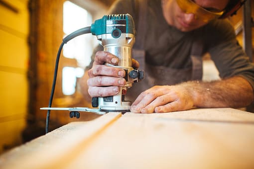 man cutting wooden board with hand-heldwood router